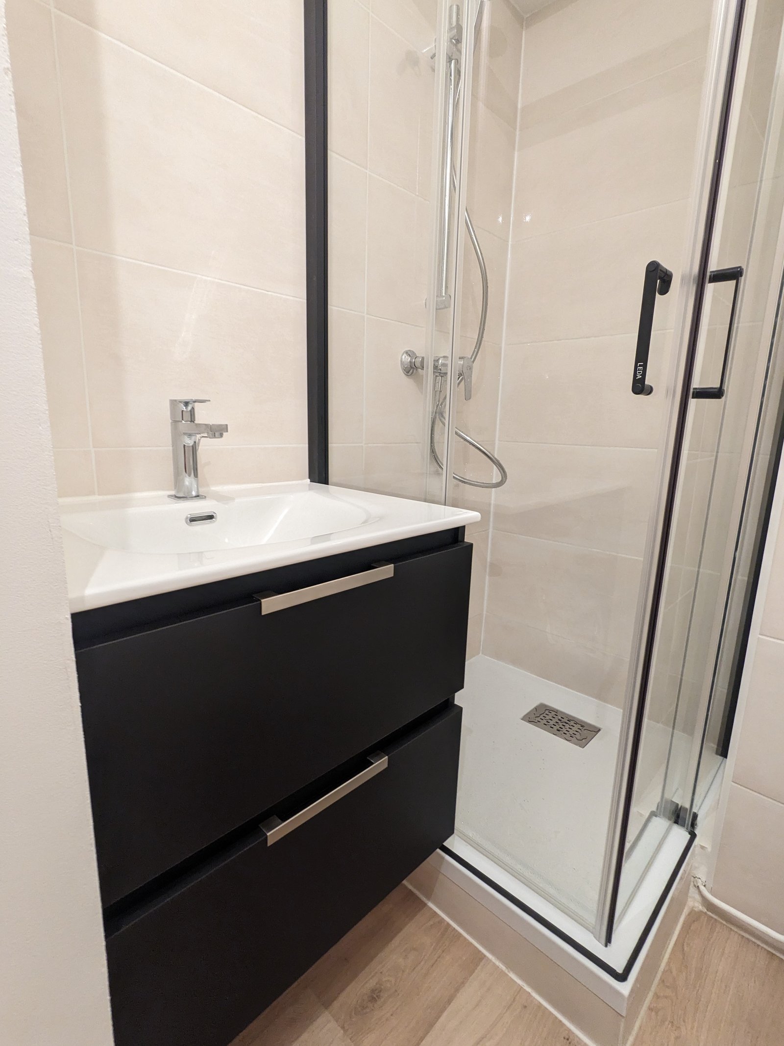 Rénovation de salle de bain à Nantes — meuble vasque noir, douche avec porte vitrée et sol PVC effet bois