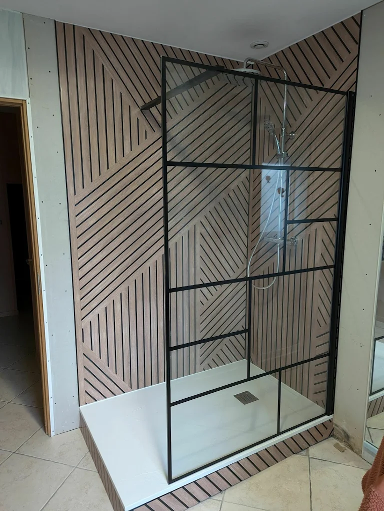 Installation d'une douche à Vertou — panneaux muraux motif géométrique bois, paroi vitrée à cadre noir et colonne de douche