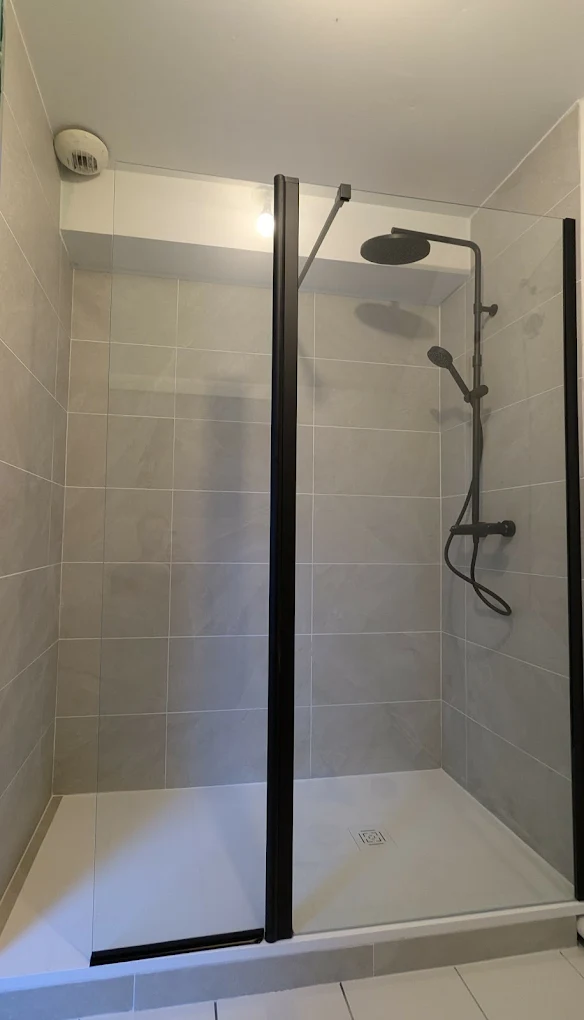 Douche moderne installée en remplacement d'une baignoire — paroi noire et carrelage gris